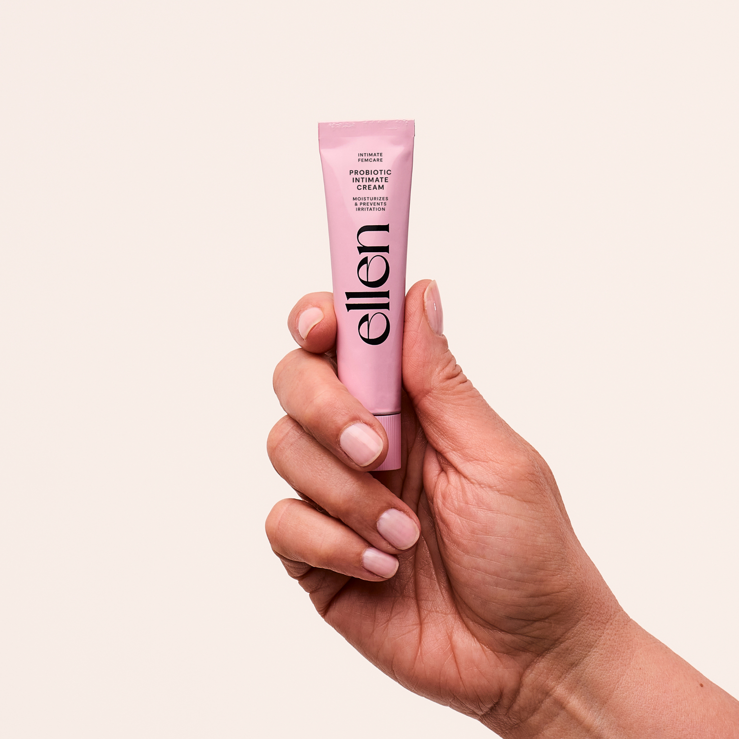 En hand med välmanikyrerade naglar håller en rosa tub märkt KÄLLA Ellen Probiotic Cream - en vårdande kräm för kvinnors intima hälsa - mot en enfärgad, ljusbeige bakgrund.